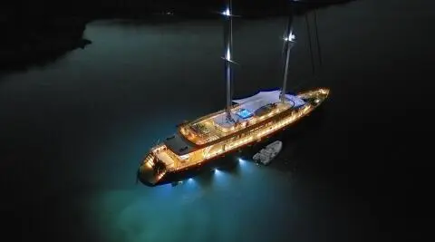Dalmatino yacht at sea at dusk, warm lights glow from deck