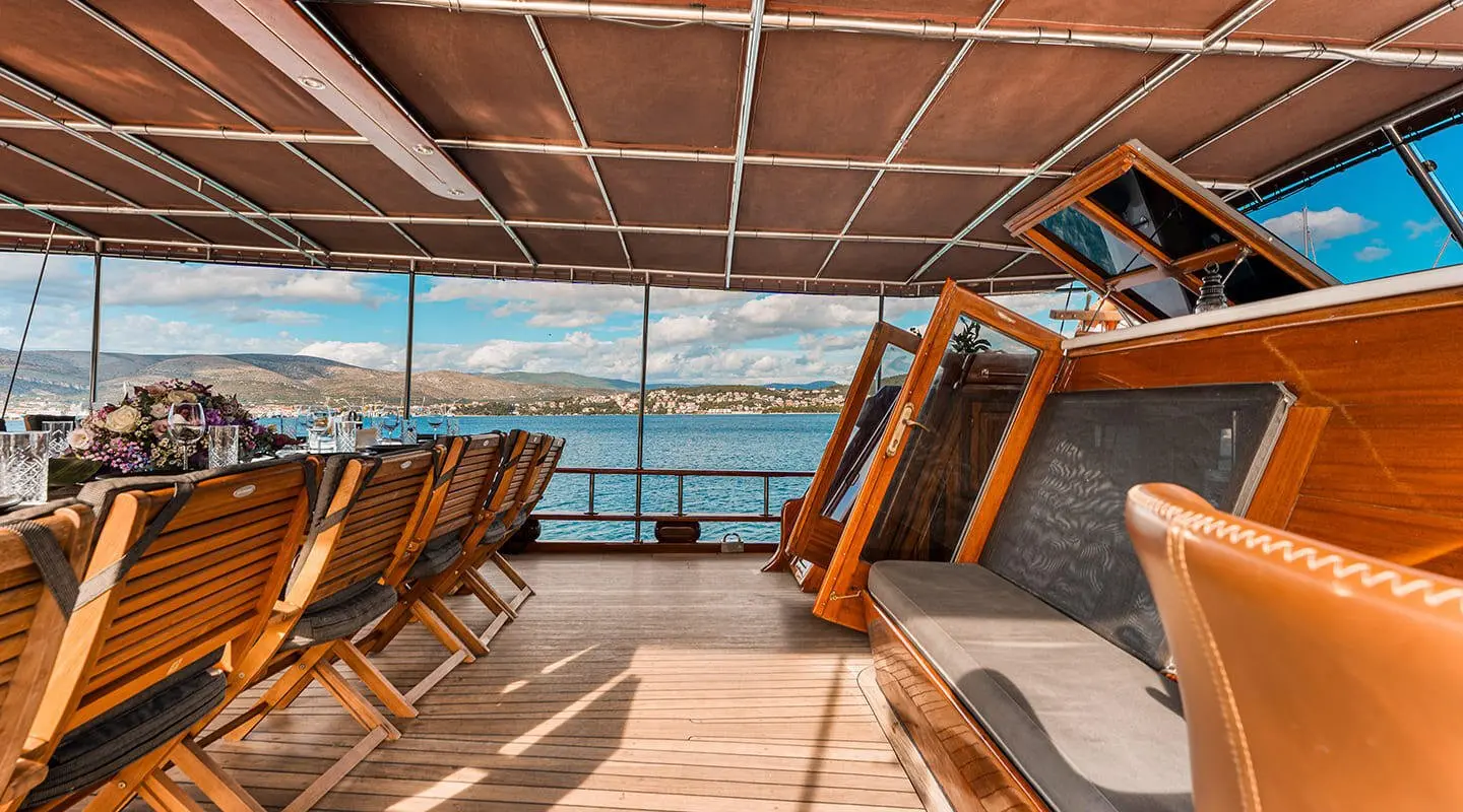 Sunlit deck of a luxury yacht with wooden seating and ocean view at sunset