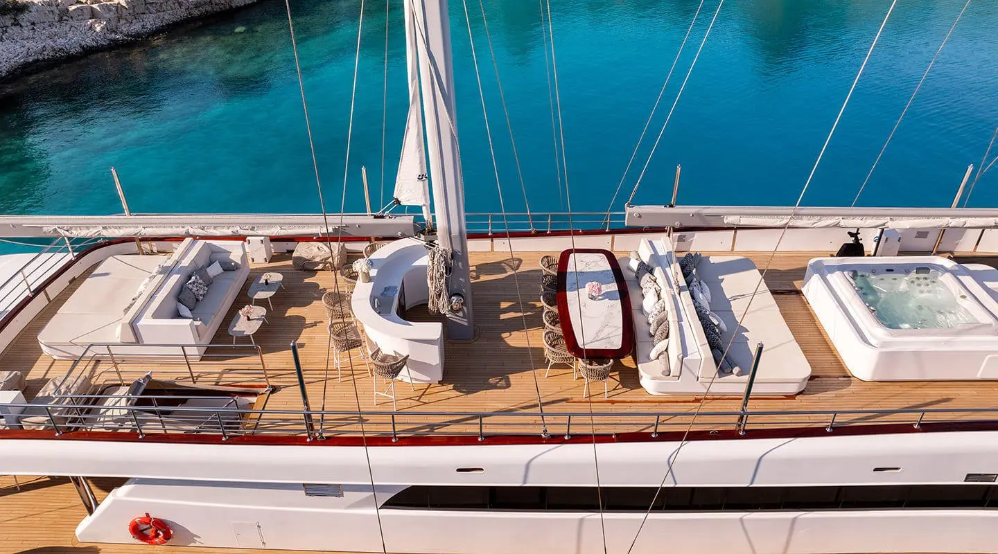 Top-down view of Nocturno yacht deck with seating, sun loungers, and railing by clear blue water