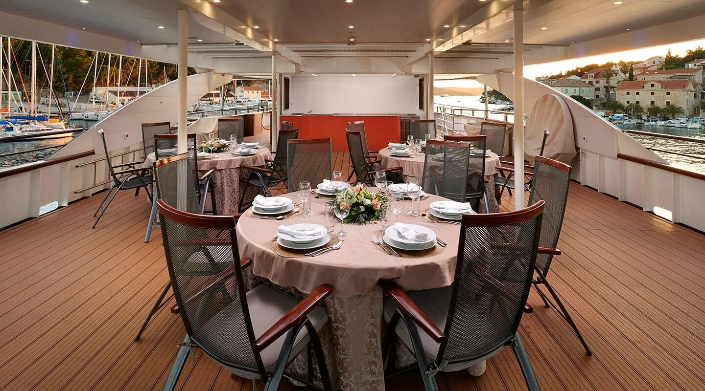 Queen Eleganza yacht dining area at sunset with table settings and chairs