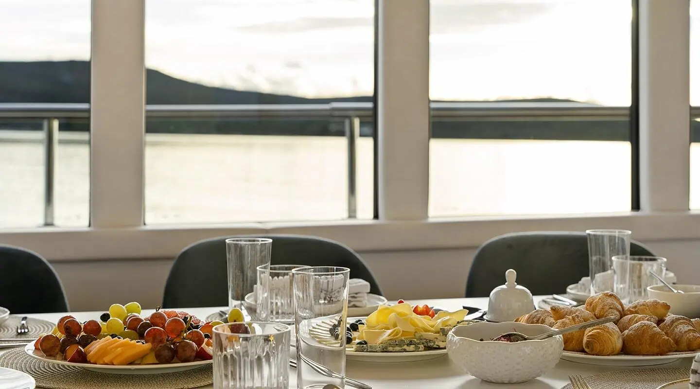 Yacht Maxita exterior view through large salon windows with dining setup