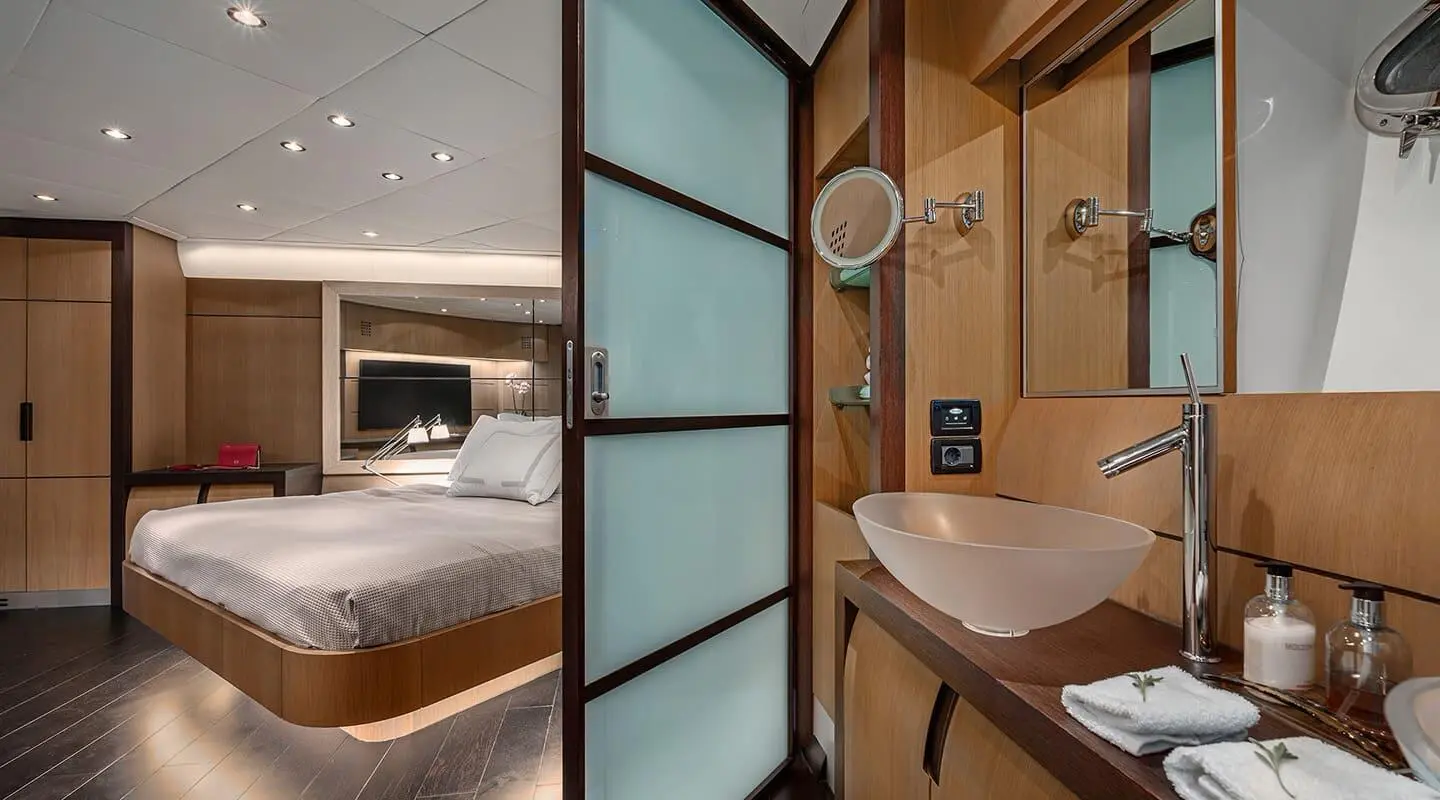 View through glass doors into a luxurious yacht cabin with bed and wooden accents
