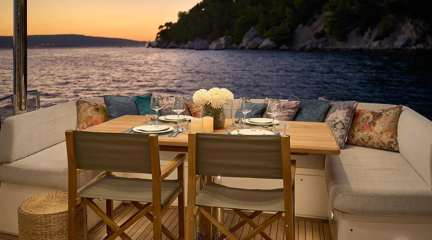 Hideaway yacht dining on deck at sunset with cushioned seating and wooden table