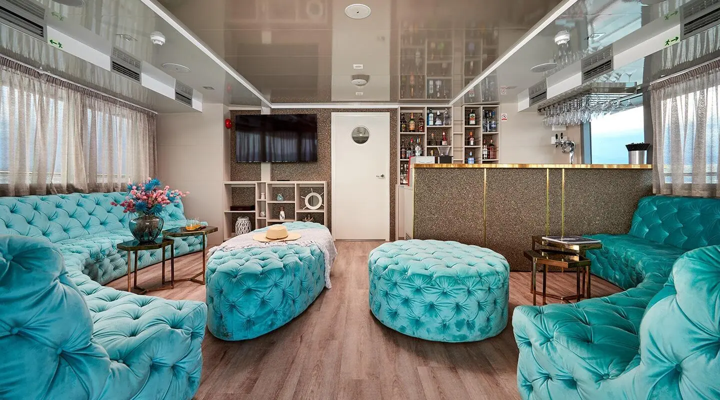 Ohana yacht salon deck: wood floor, two teal ottomans, shelving, and seating areas