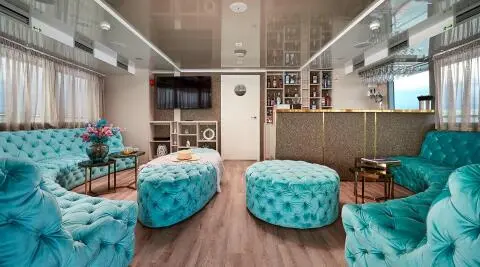 Ohana yacht salon deck: wood floor, two teal ottomans, shelving, and seating areas