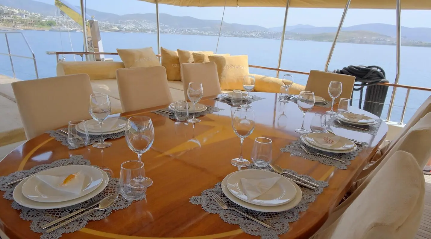 Queen Of Sea luxury yacht dining area set with plates, glasses, and sunset view