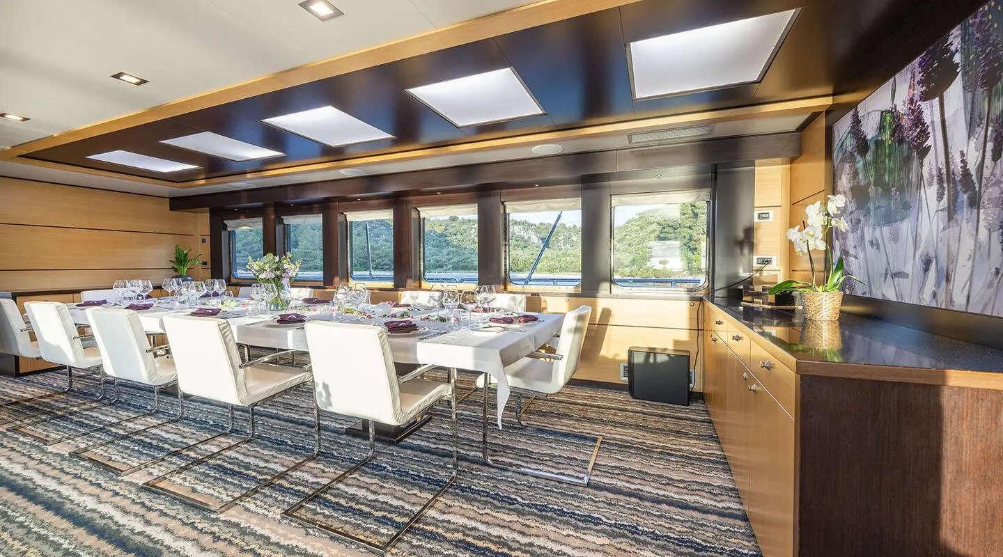Navilux yacht dining salon with large windows, table set for eight, warm overhead lighting