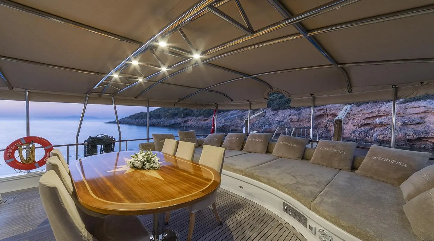 Aft deck of Queen Of Sea gulet showing curved seating, wooden table, and shaded canopy