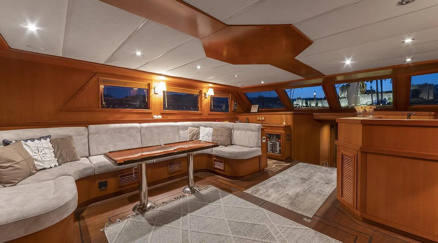 Luxurious yacht salon with wooden cabinetry, beige seating, and ceiling windows