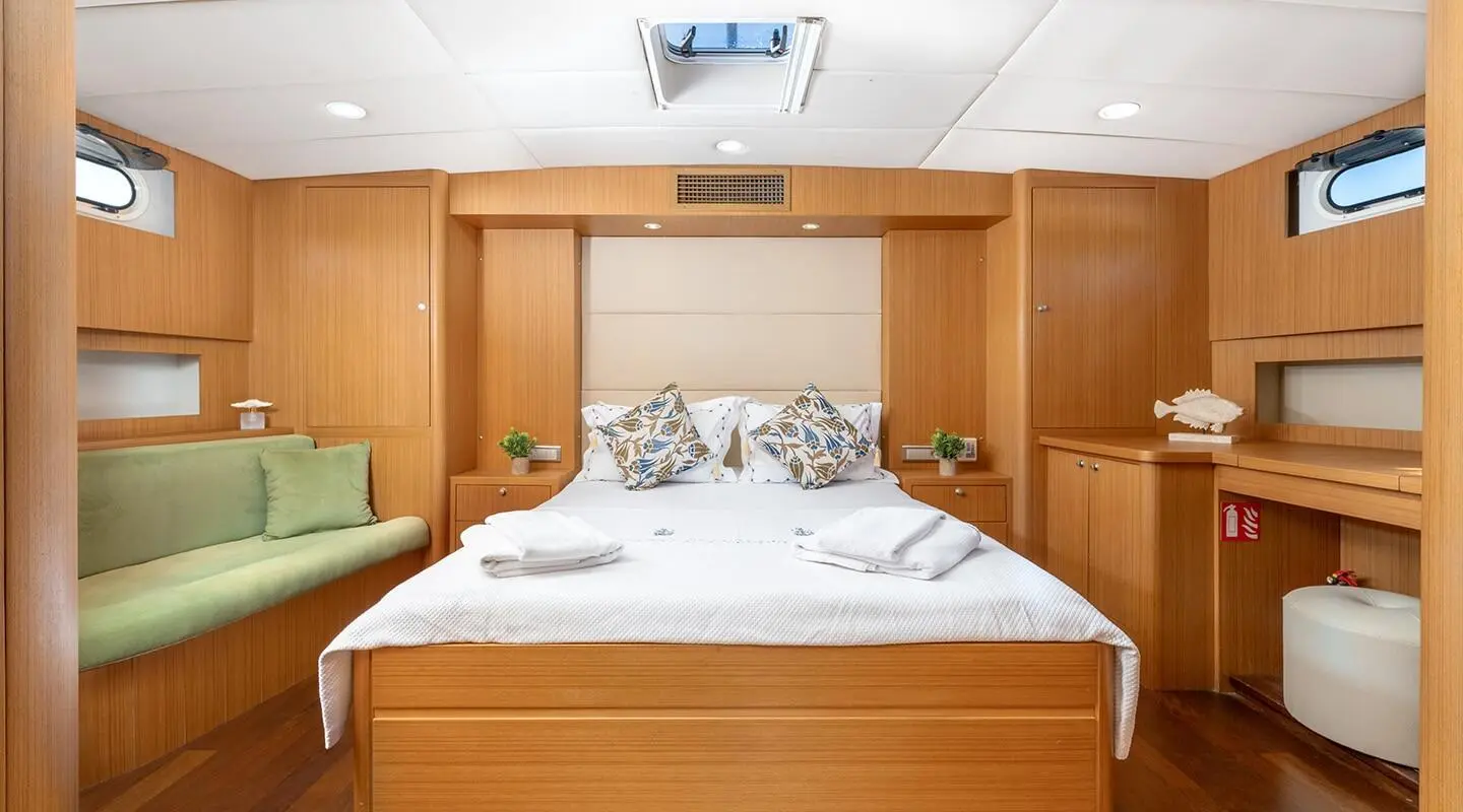Bedroom inside a wooden-panel yacht with a white bed and decorative pillows.
