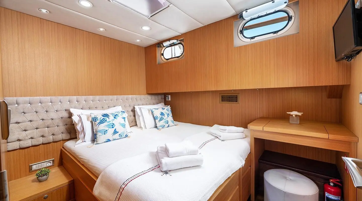 Artemis yacht interior with bed, wooden cabinetry, and window view at dusk