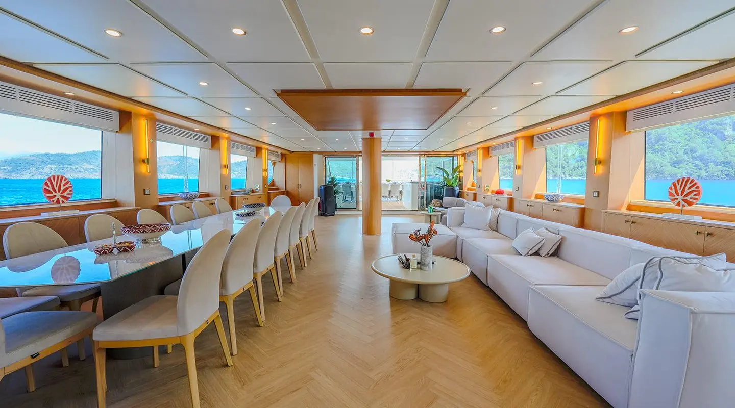 Inside lounge with long dining table, white seating and sea view windows