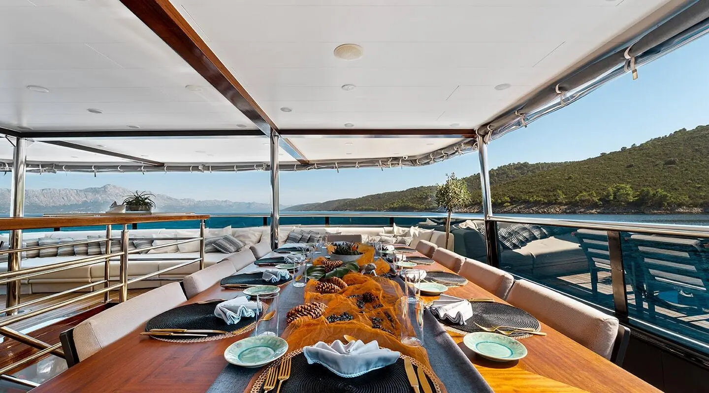 Yacht Freedom dining table set with plates and chairs under shaded deck