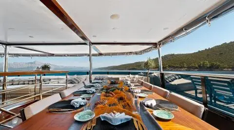 Yacht Freedom dining table set with plates and chairs under shaded deck