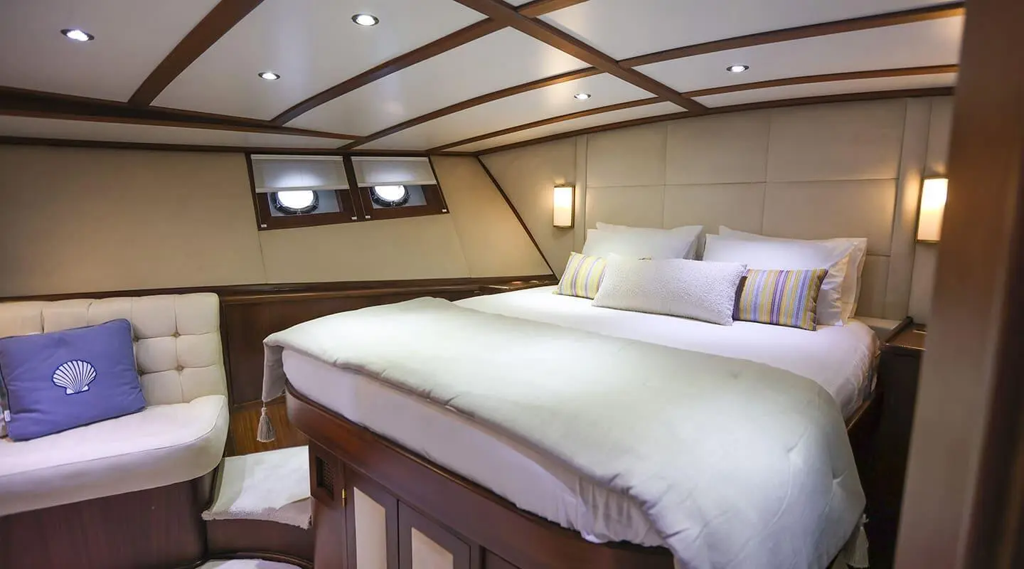 Gazella gulet master cabin interior with large bed, portholes, and wooden beams