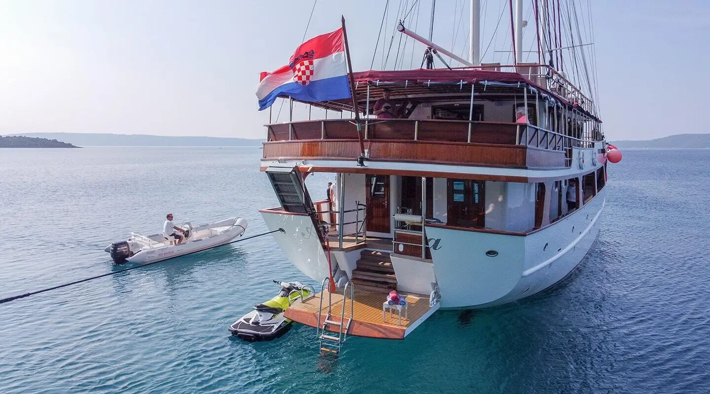 Yacht Amorena anchored near clear blue water with a small tender nearby