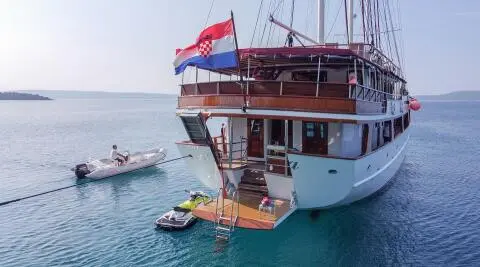 Yacht Amorena anchored near clear blue water with a small tender nearby