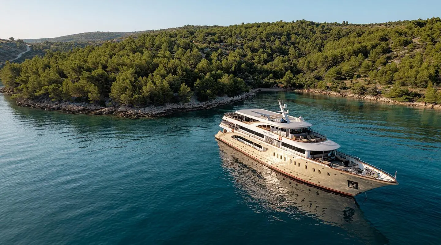 Queen Eleganza yacht anchored near a forested coastline with clear blue water