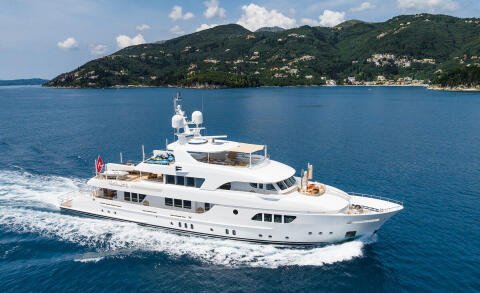 White luxury motor yacht sailing on blue sea, with green hills in background