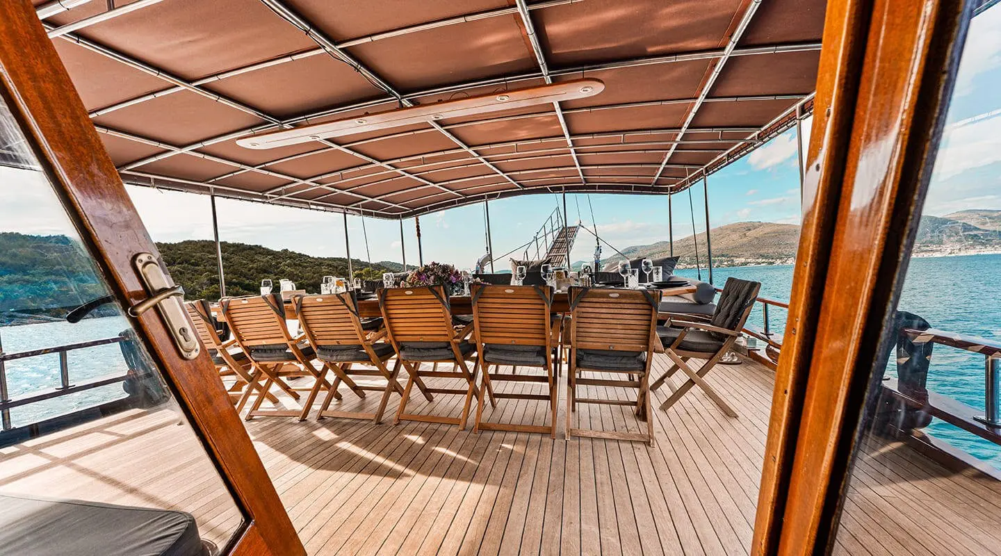 Dining area on a yacht with chairs, wooden deck, and a sunshade over us