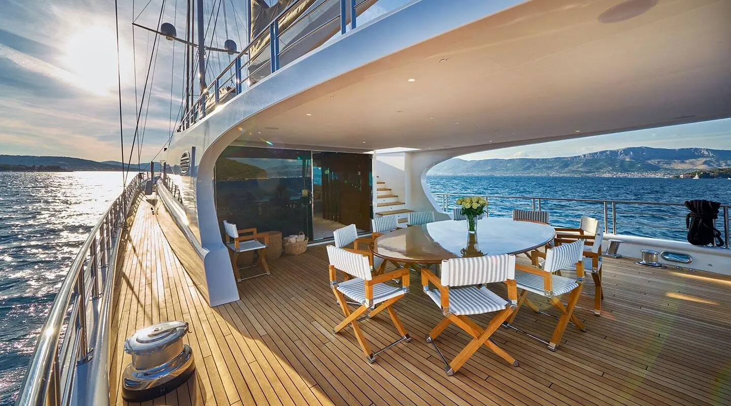 Acapella yacht deck dining area with table and chairs on wood deck by ocean