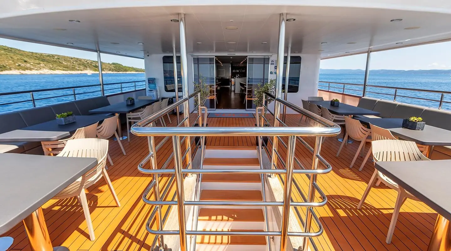 Yolo yacht deck lounge with seating, stairs, rails, and ocean view at sunset