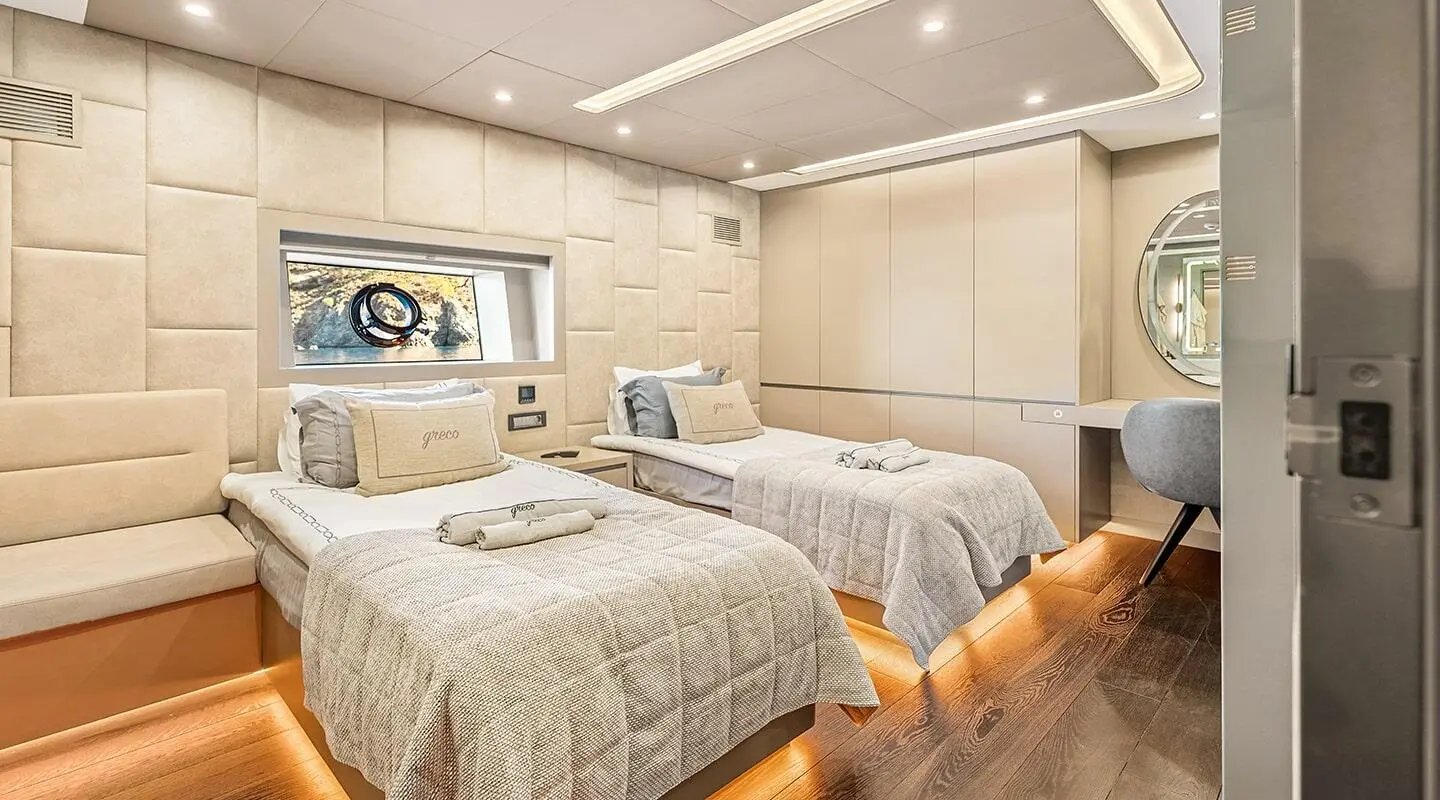 Twin-berth yacht cabin on North Wind with porthole, wood cabinets, and beige bedding.