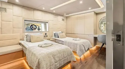 Twin-berth yacht cabin on North Wind with porthole, wood cabinets, and beige bedding.