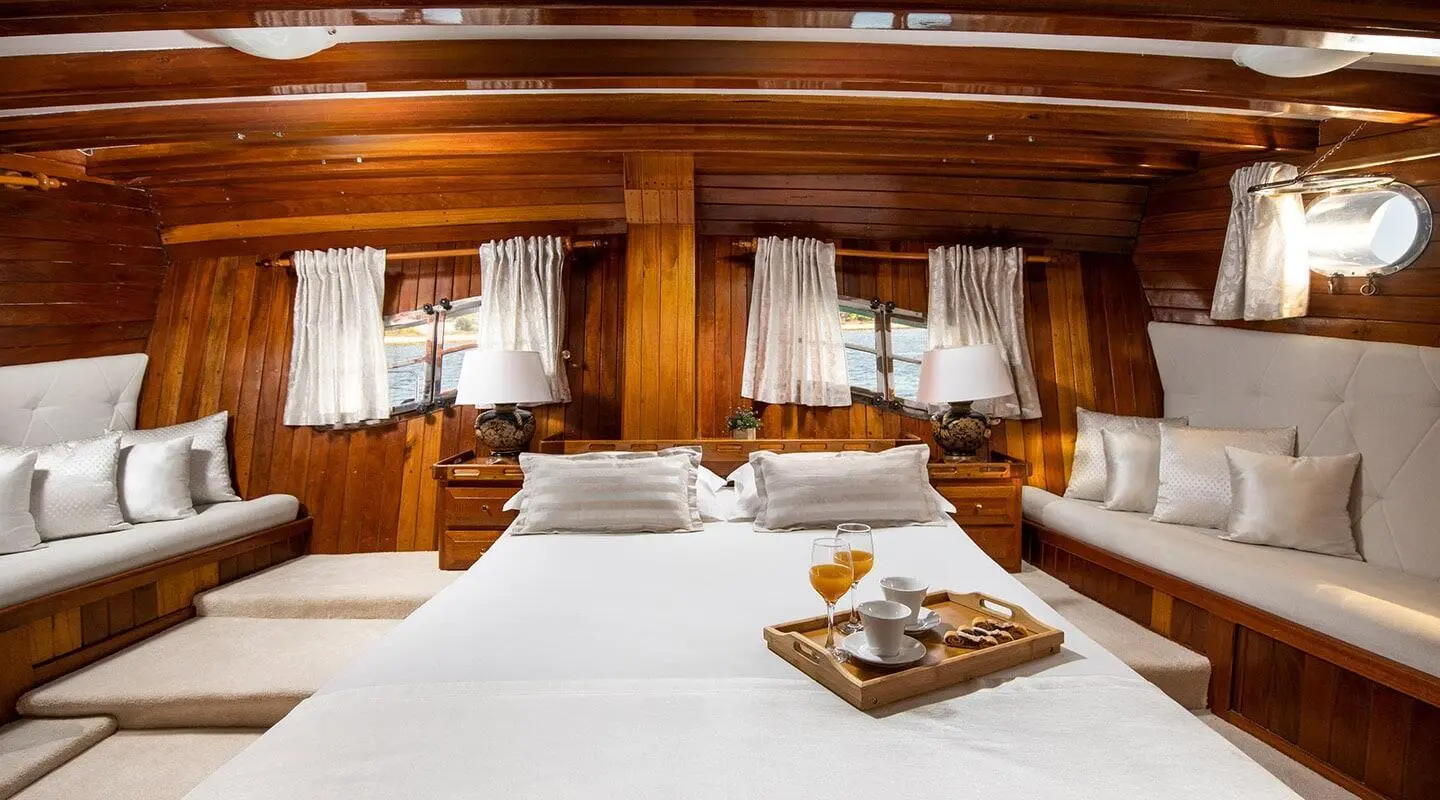 Andi Star yacht interior with polished wood, portside bed and white linens