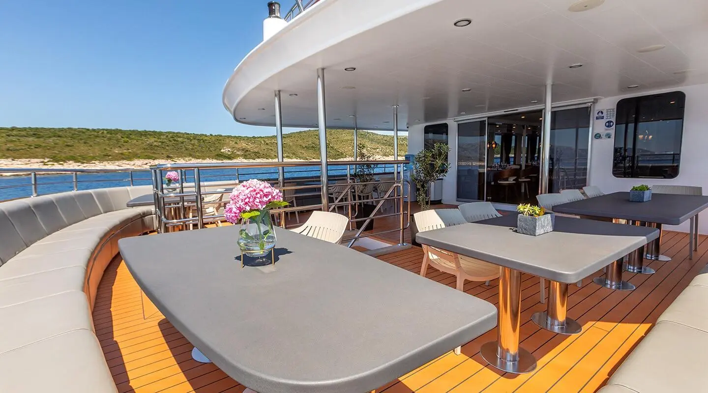 Yacht Yolo lounge deck with seating, table, sunlit water view at dusk