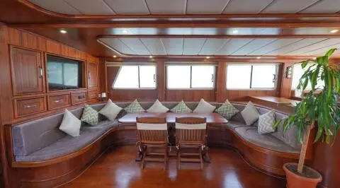 Luxurious yacht saloon with cream seating, wooden floor, windows, and table
