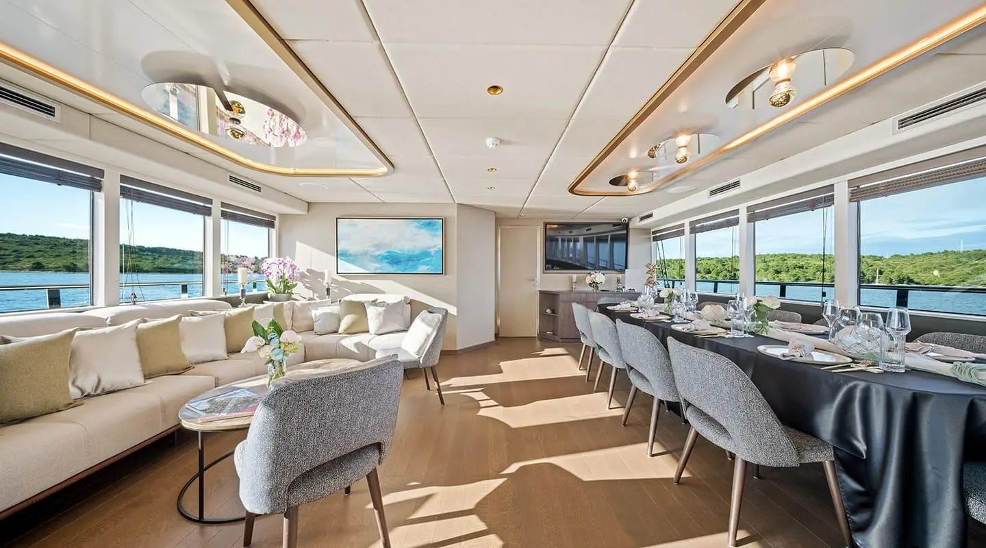 Luxurious yacht salon with dining area, large windows, and beige seating