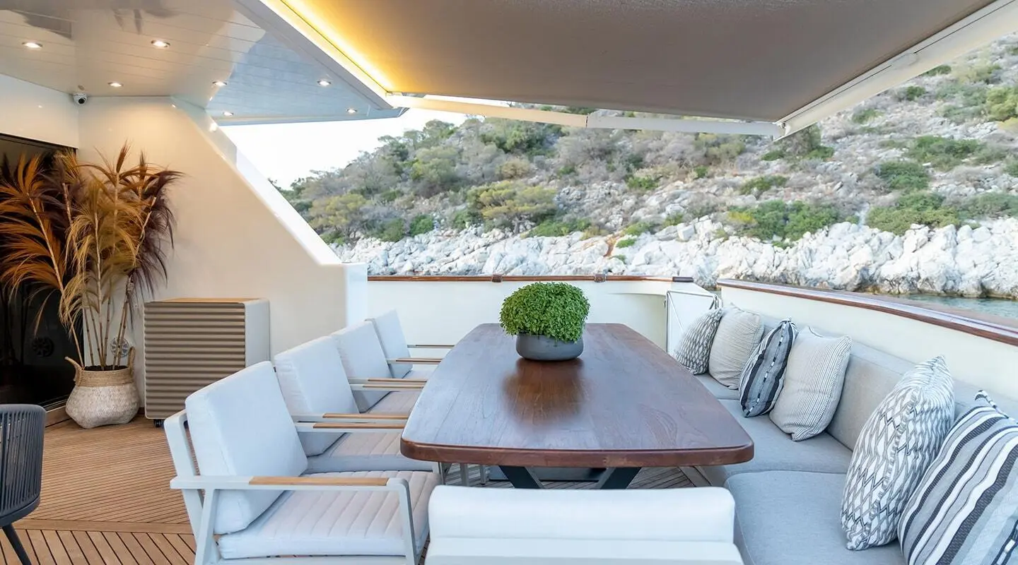 Aquila yacht deck seating area with a wooden table and white cushions