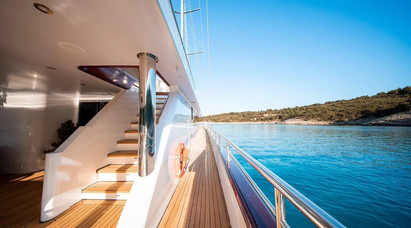View along the yacht Nocturno deck with polished wood, railing, and blue sea