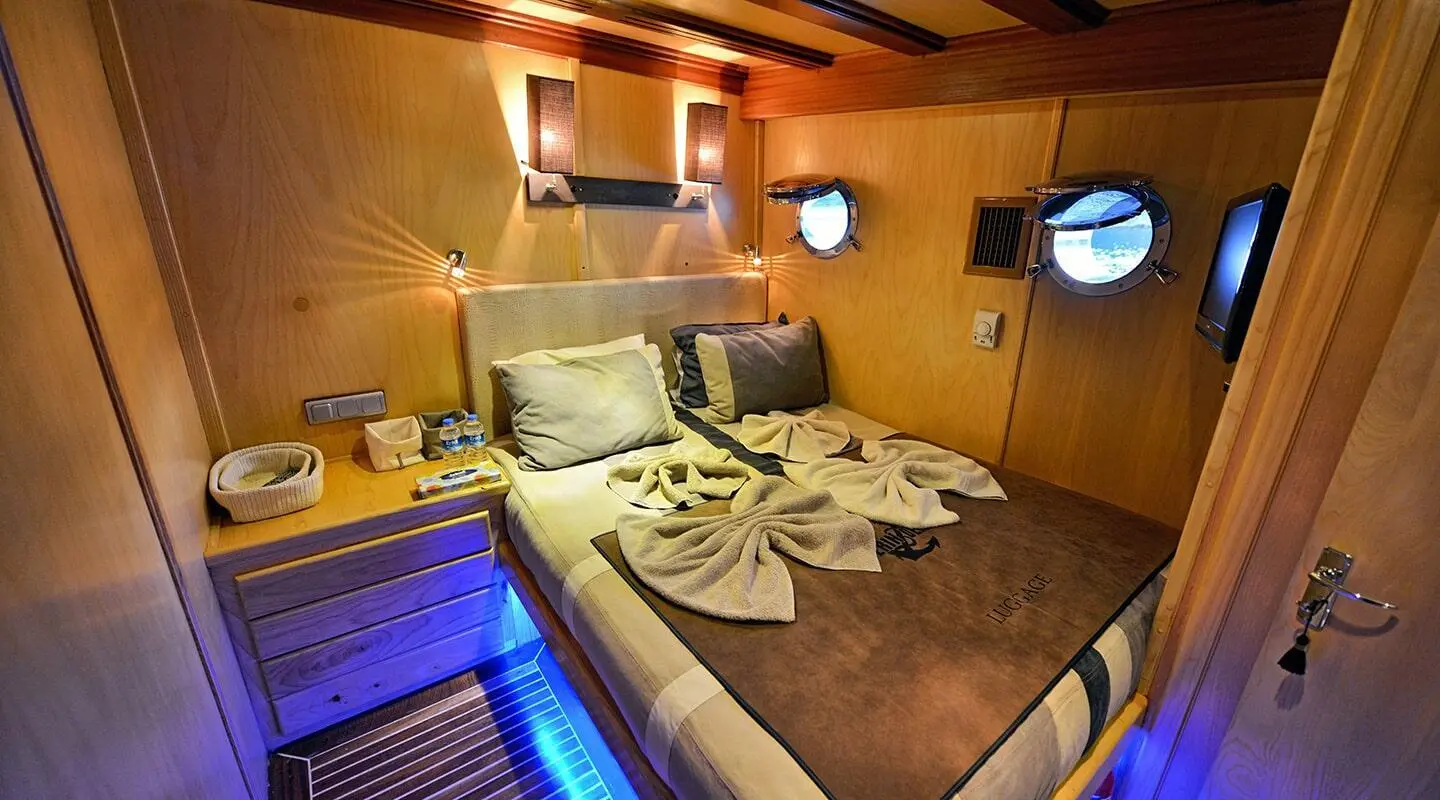 Interior cabin on luxury gulet: wooden walls, bed with folded towels, soft lighting