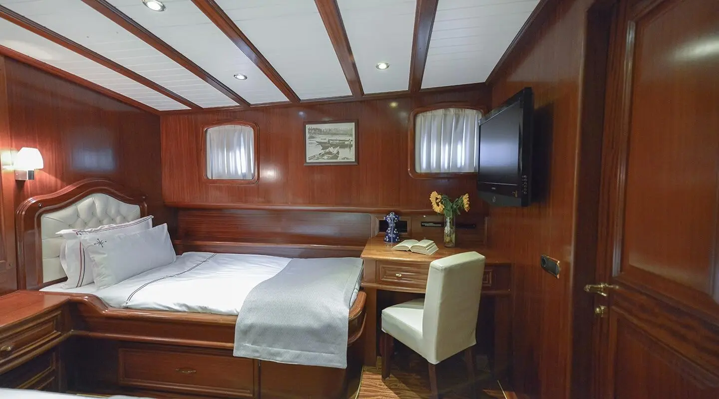 Interior of a yacht cabin with wooden panels, two twin beds, and a desk