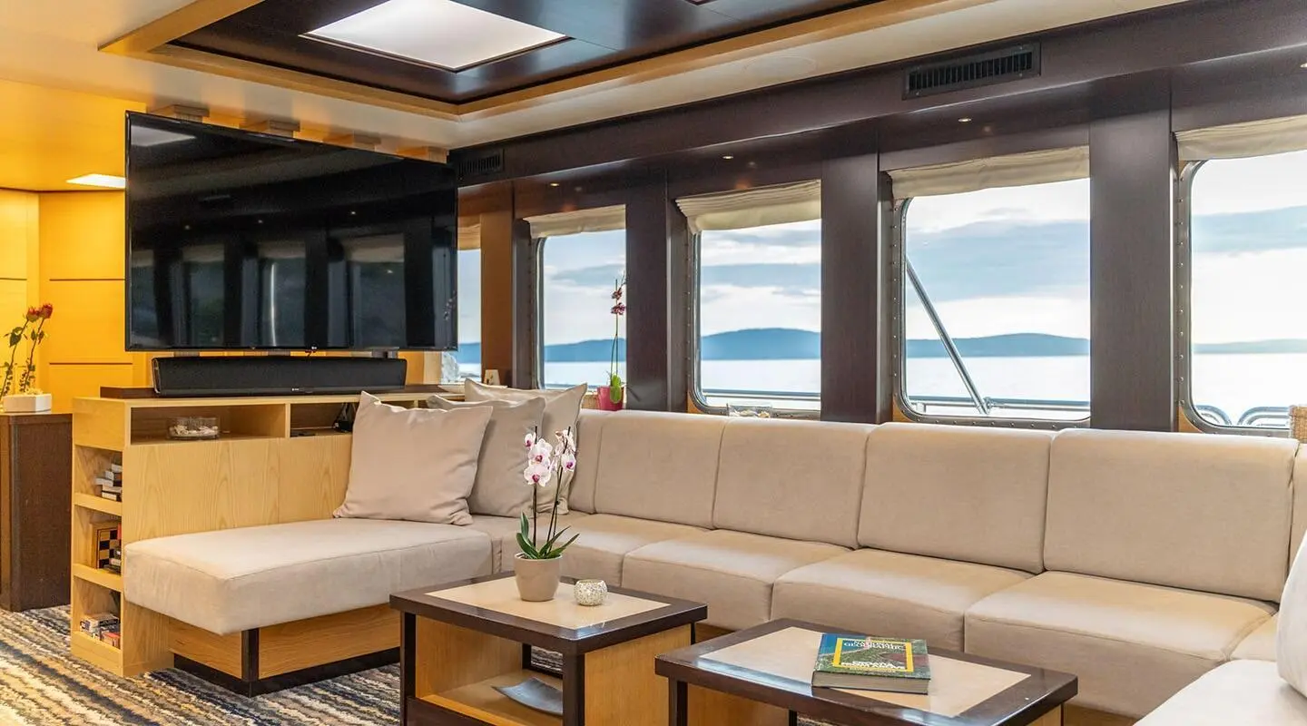 Interior lounge with large sofa, TV, and windows overlooking water