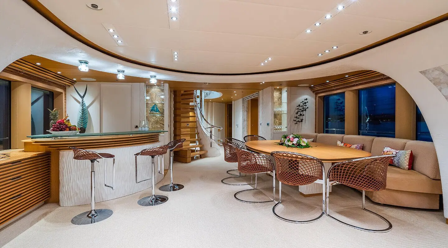 Spacious yacht salon with curved seating, wooden table, and chandelier lighting
