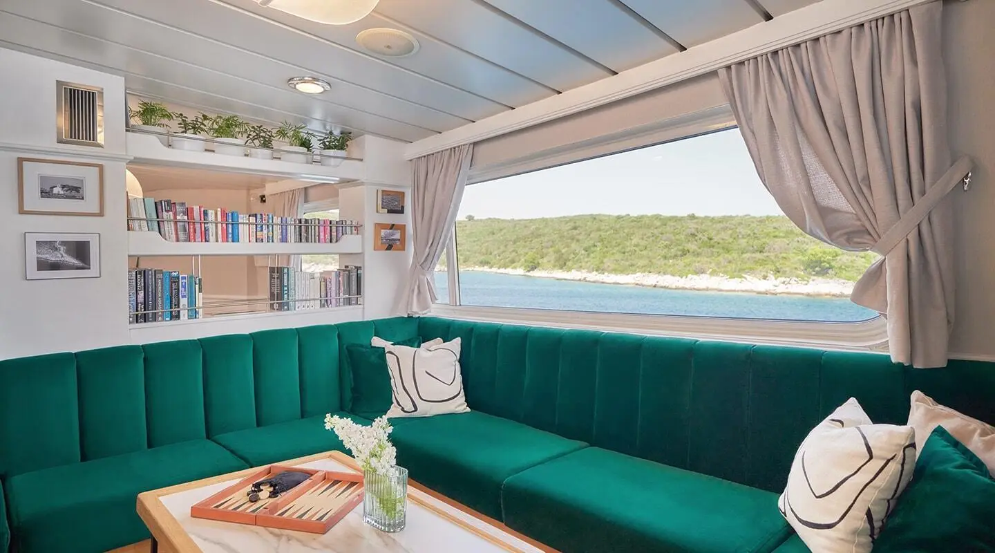 La Perla yacht lounge area with teal cushioned seating and a window view