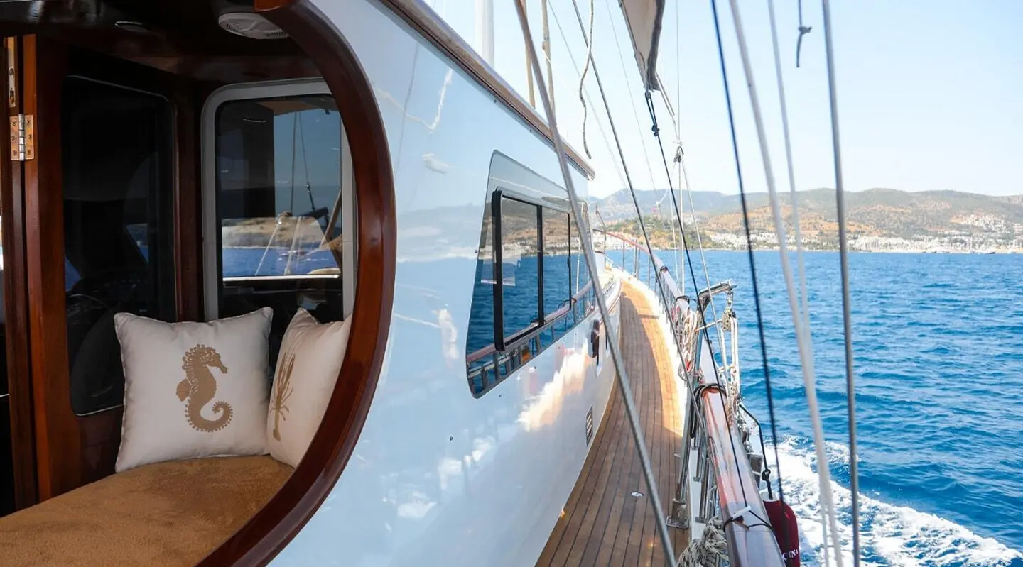 Side deck of Ulucinar gulet, white hull, windows, railings by blue sea