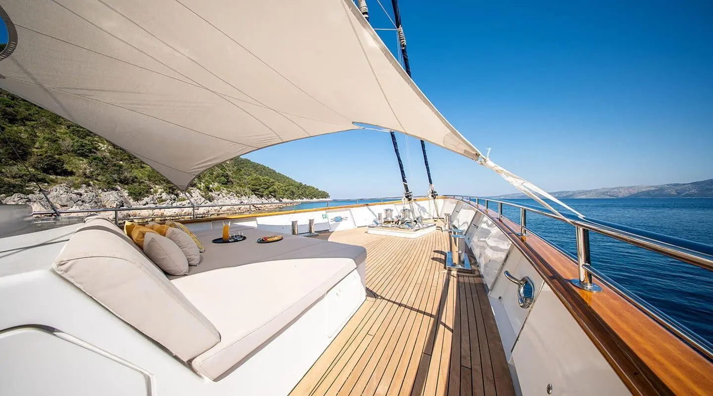 Sundeck with cushioned seating under a sunshade, sea and shoreline in the background