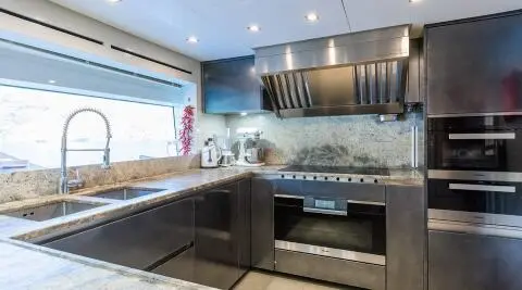Takara One yacht kitchen with stainless steel appliances and dark cabinetry