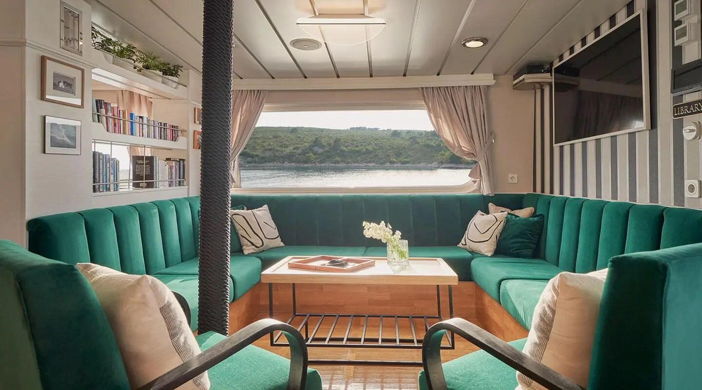 La Perla yacht interior lounge with teal seating and wooden table during sunset