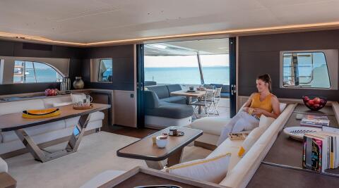 Daiquiri yacht interior: bright salon with cream seating, glossy wood table, open aft deck view of sea