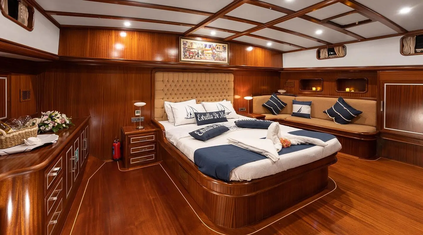 Estrella De Mar yacht interior with a large bed, porthole lighting, and wooden paneling