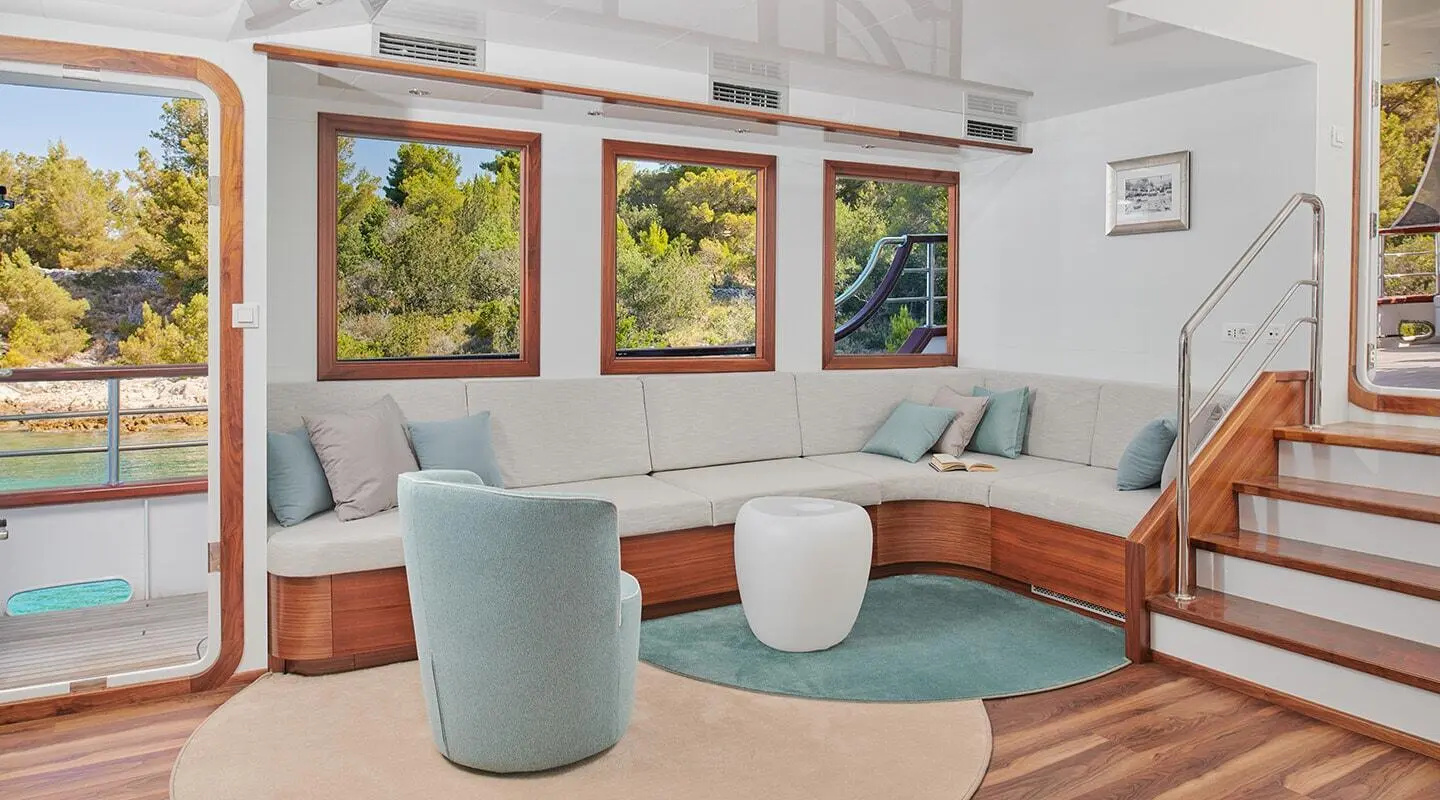 Corsario yacht interior with curved sofa, round coffee table, and windows showing greenery
