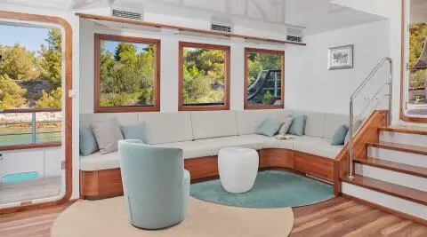 Corsario yacht interior with curved sofa, round coffee table, and windows showing greenery