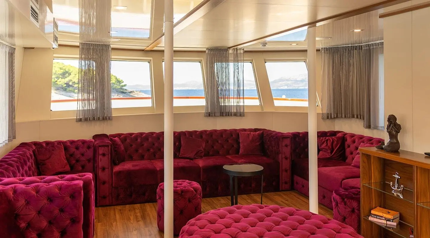 Interior lounge with red velvet seating, wooden panels, large windows showing sunset