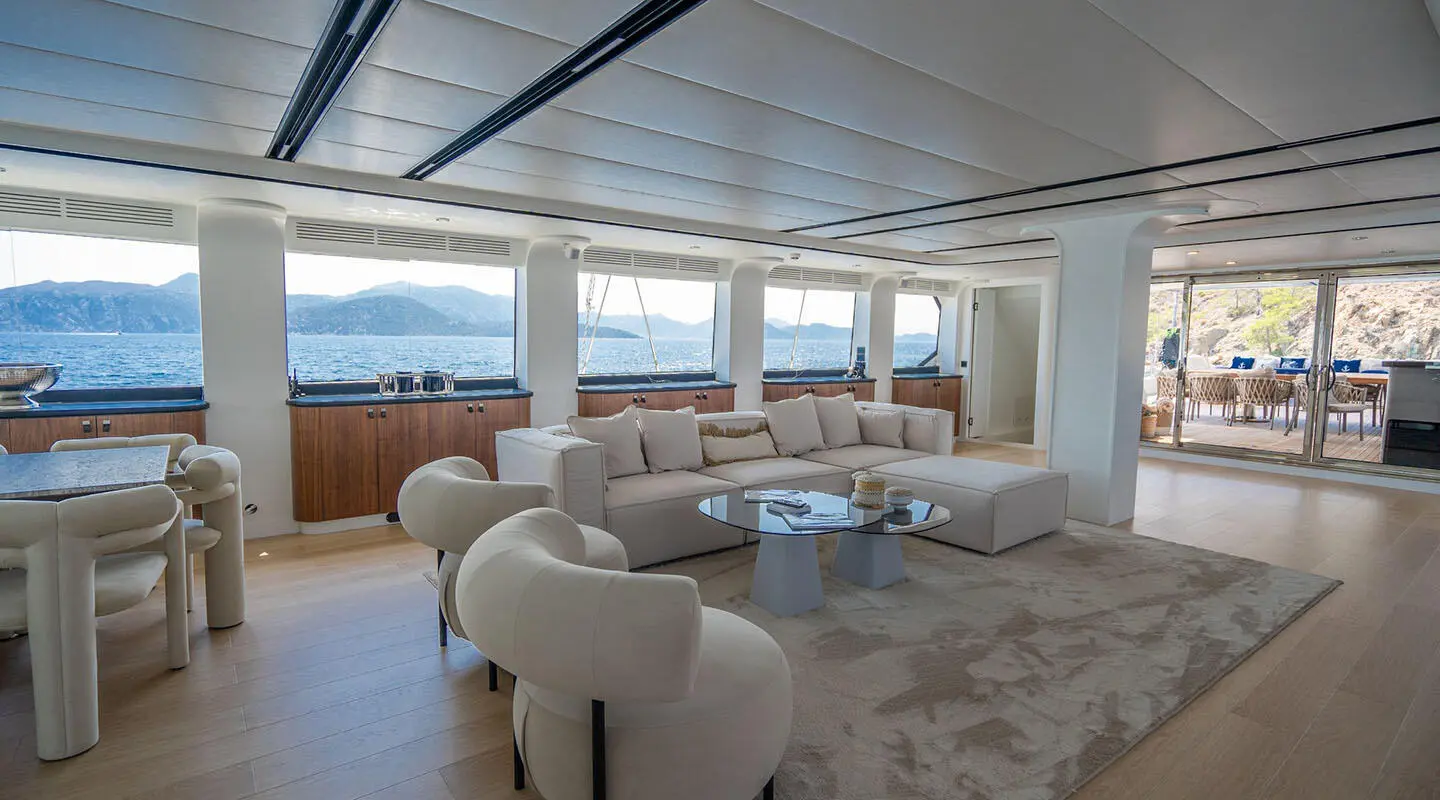 Interior yacht salon with white seating, glass windows, and sunset view