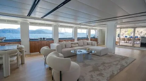 Interior yacht salon with white seating, glass windows, and sunset view